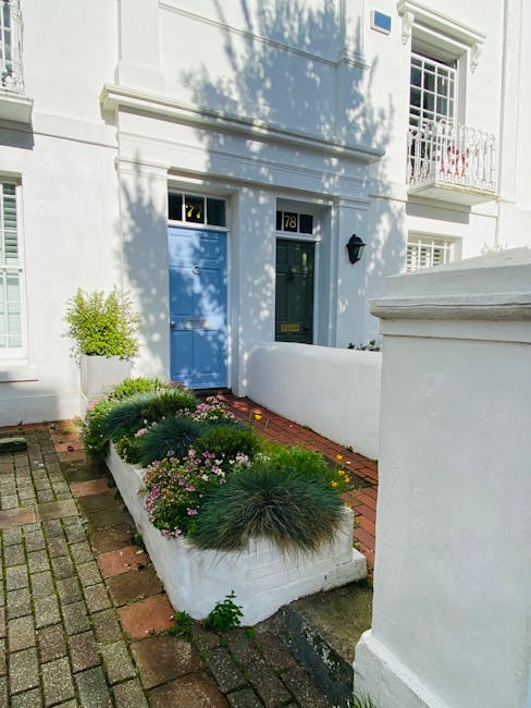 A small front garden area in front of a white residential building, featuring a narrow brick pathway leading to a blue front door marked with the number 78. The garden bed along the path contains neat